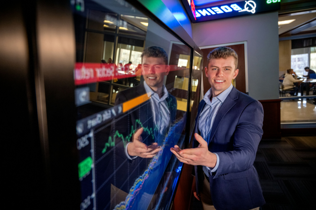 Nick Lloyd standing in front of a TV screen in the Dykman Financial Trading room.